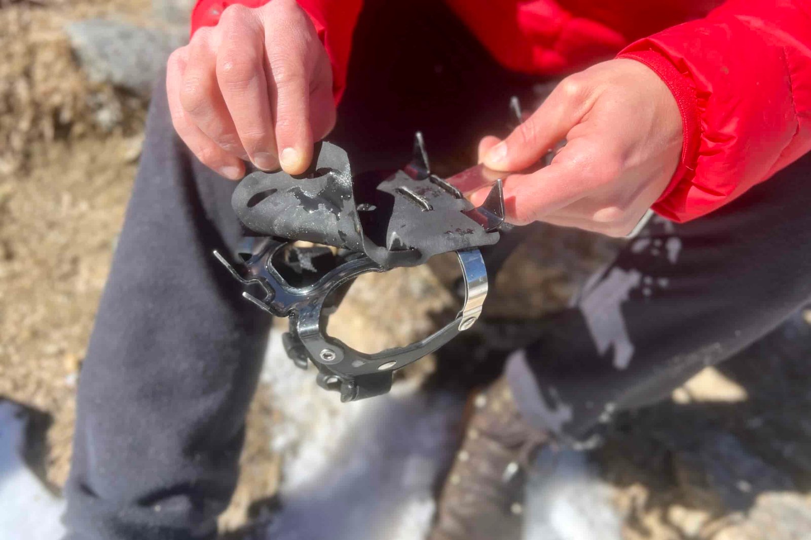 A close up of a hiker's hands pulling the snow skins off of a pair of trail crampons.