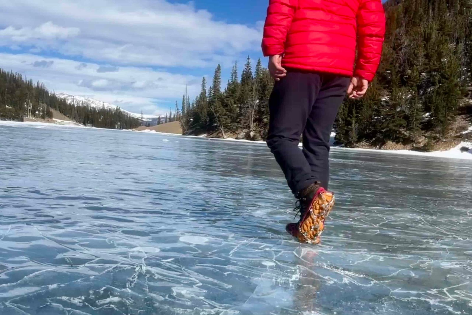 A hiker walks away from the camera on a frozen lake while wearing a pair of ice cleats.