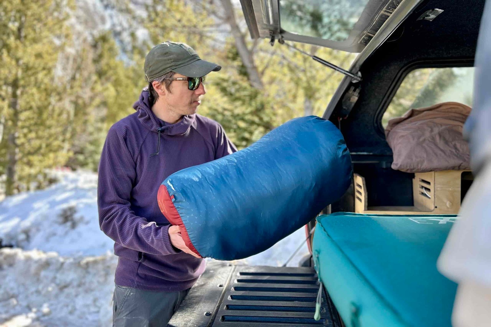 A man lifts a sleeping bag in a stuff sack to put in the back of a truck.