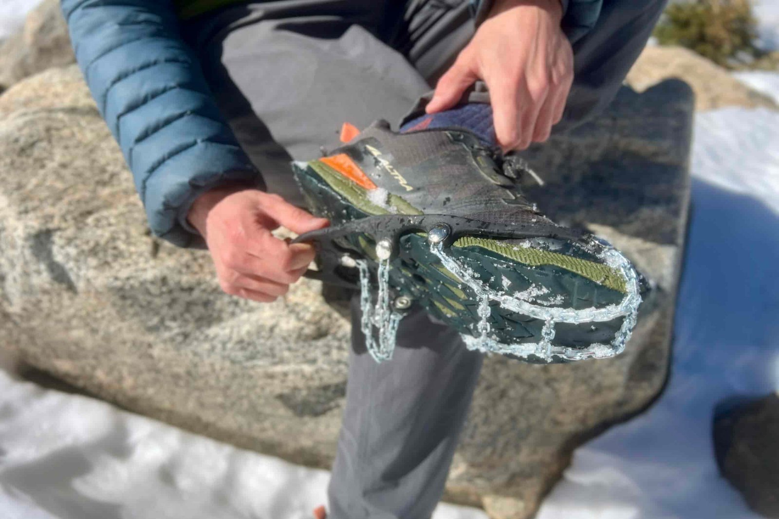 A hiker sits on a rock and pulls a pair of ice cleats from his feet.