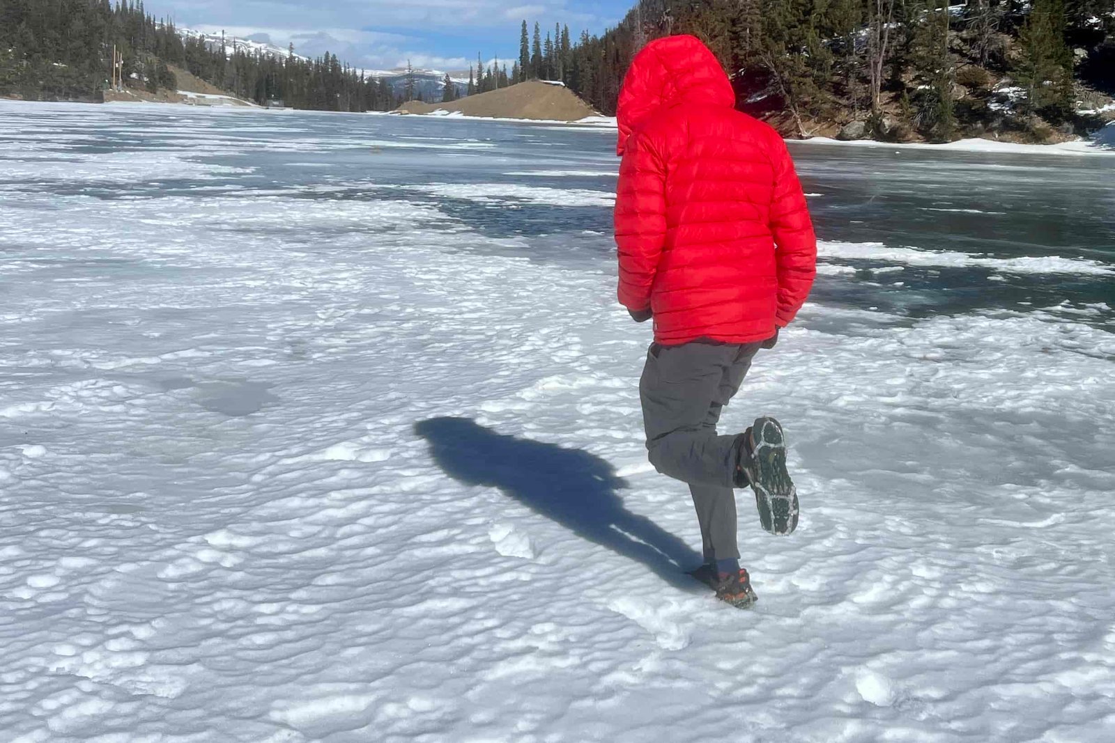 A person runs away from the camera on a frozen lake while wearing ice cleats.