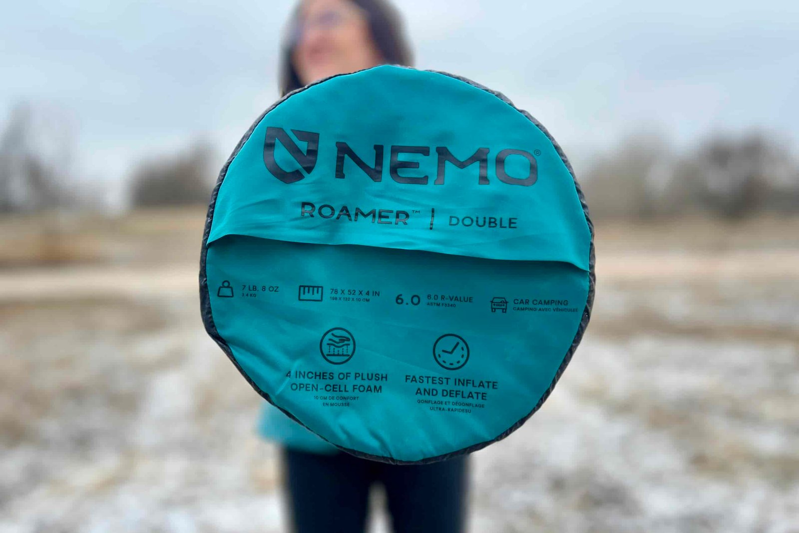 A person holds out a sleeping pad with the bottom visible, showing off infographics, the brand name, and other information printed on the bottom.