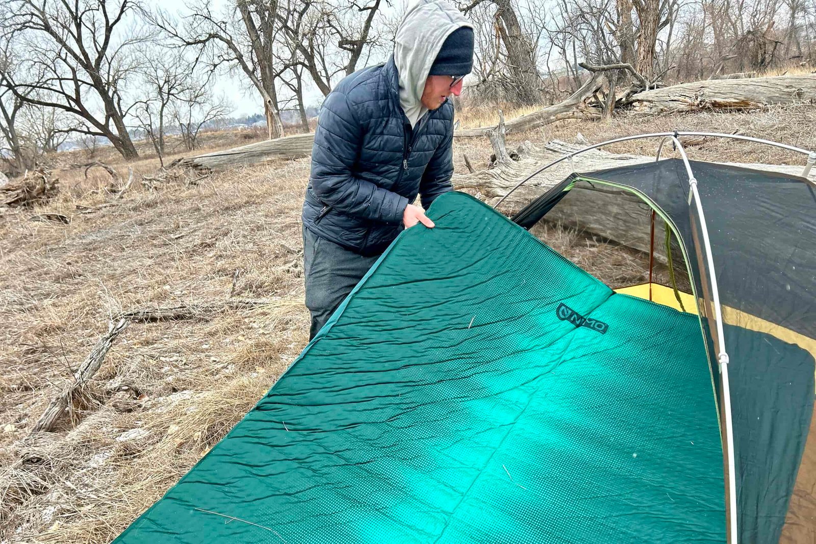 A man slightly folds a camping mattress to fit it into a camping tent.
