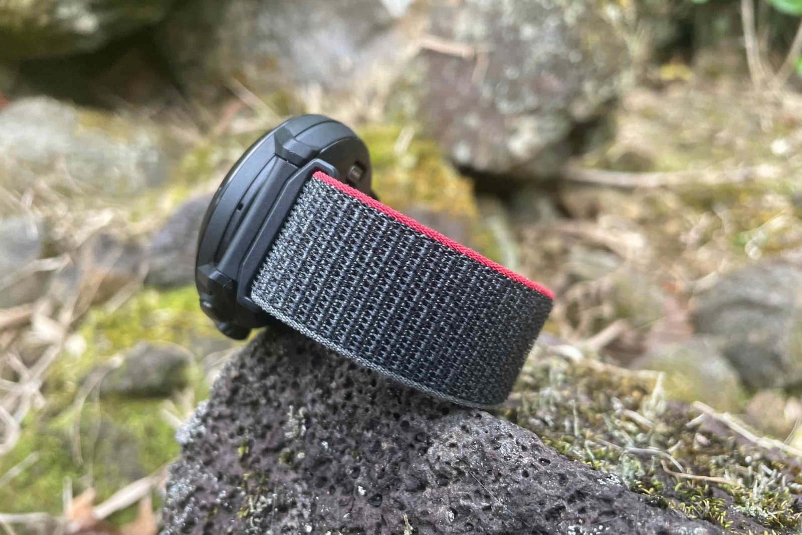 A closeup of a GPS watch on a mossy rock showing the nylon watch band.