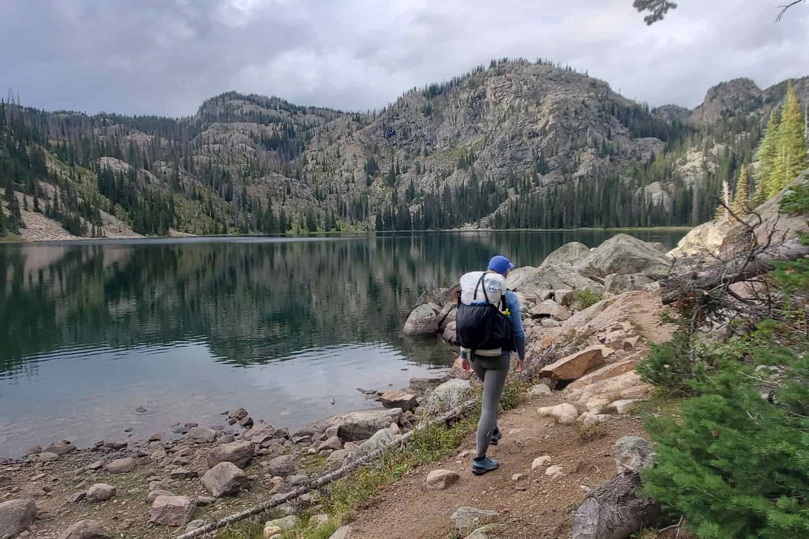 A woman hikes along a mountain lake.