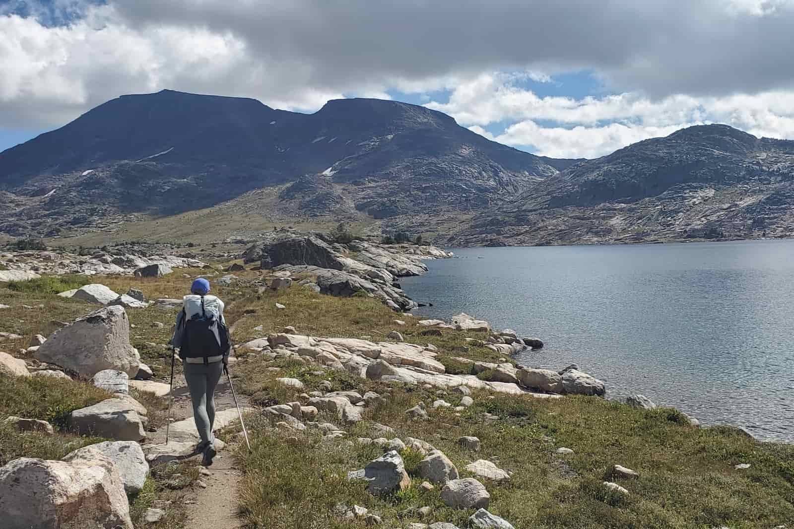 A woman hikes through an alpine landscape along a lake.