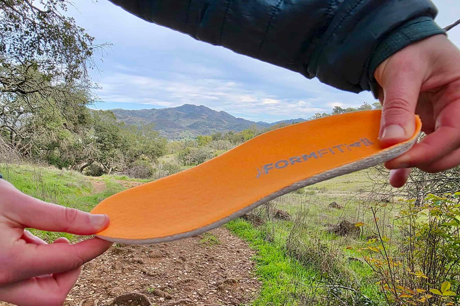 Hiker holding up the thick insole of the Saucony Peregrine, with a mountain in the background.