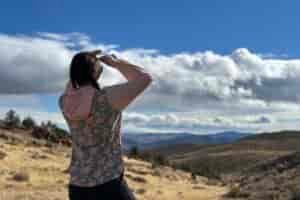 Woman in floral sun shirt looking out at view of foothills in high desert detting