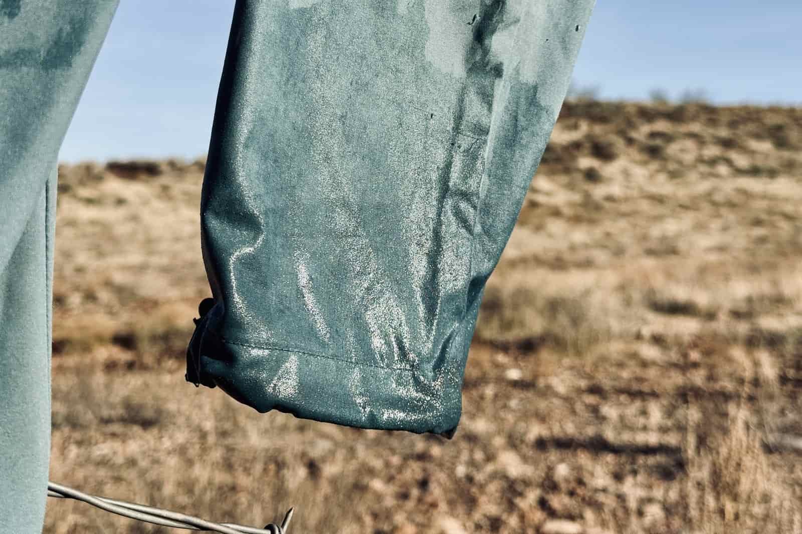 Close up of the wet hem of the Baleaf pants handing off of a fence to dry. The background is a dry, grassy desert.