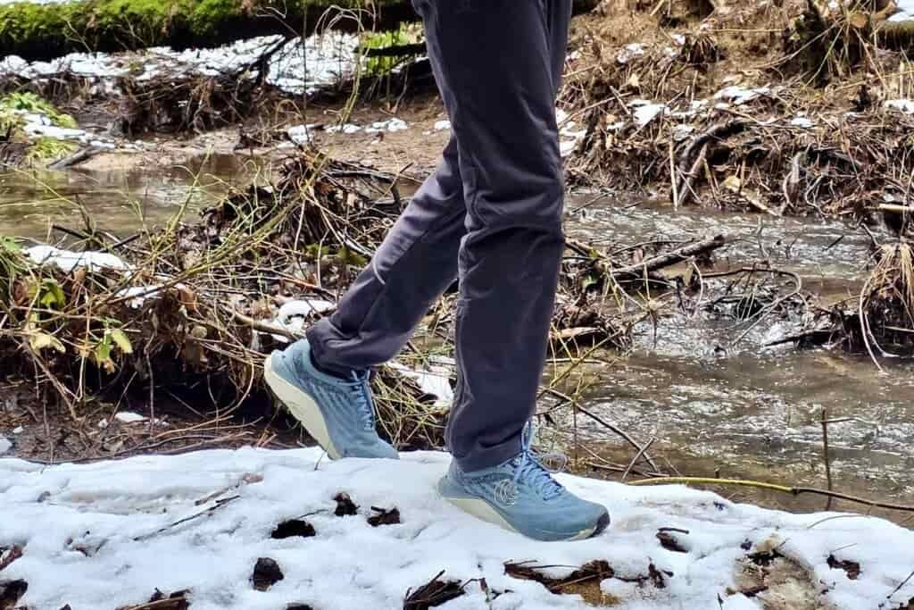 A person walks through the snow along a creek.