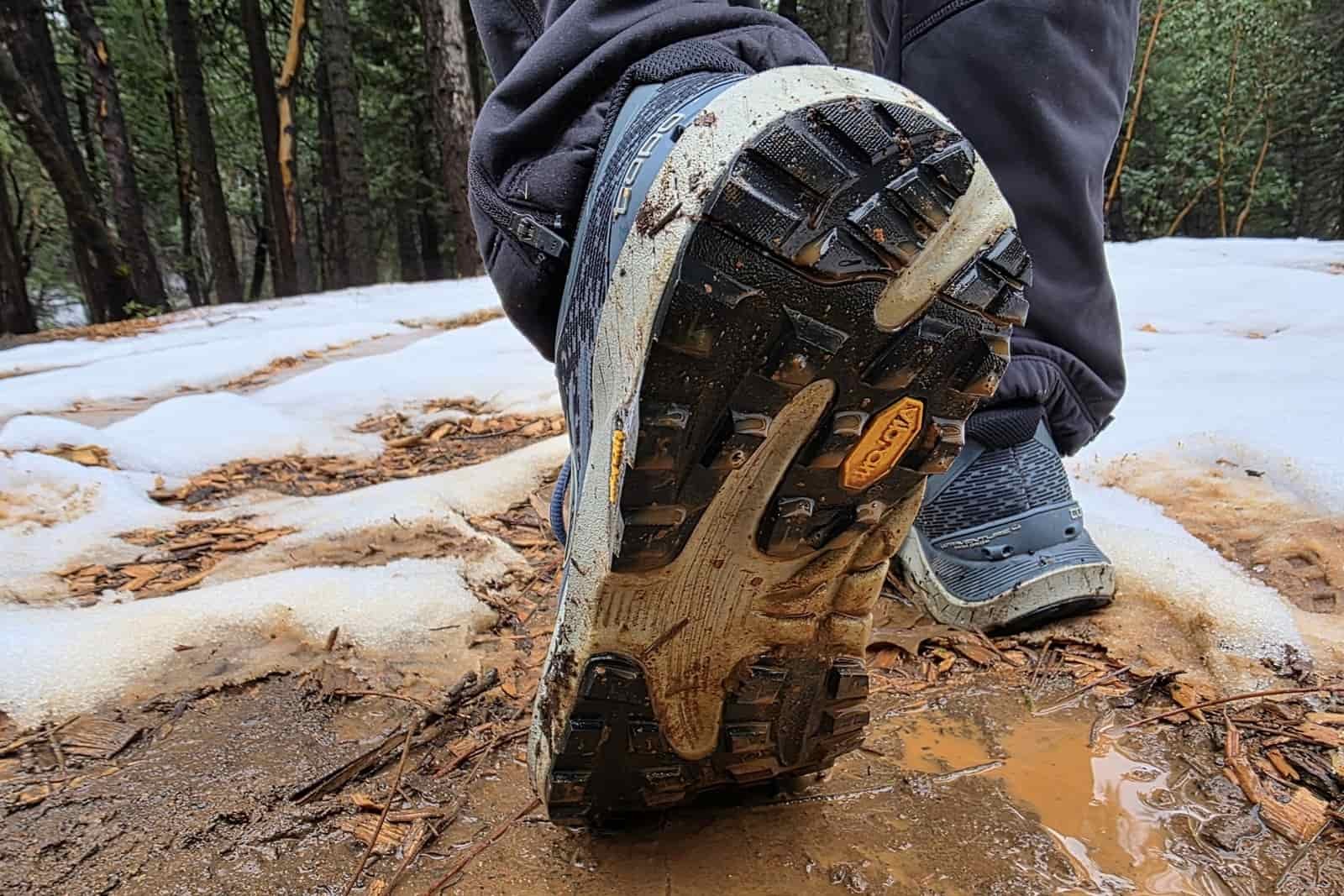 Close-up showing the tread of a hiking shoe over muddy/slushy terrain.