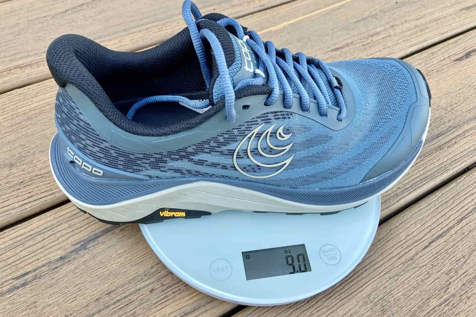 Close-up showing the weight of one Topo Ultraventure 4 shoe on a kitchen scale. It weighs 9 ounces.