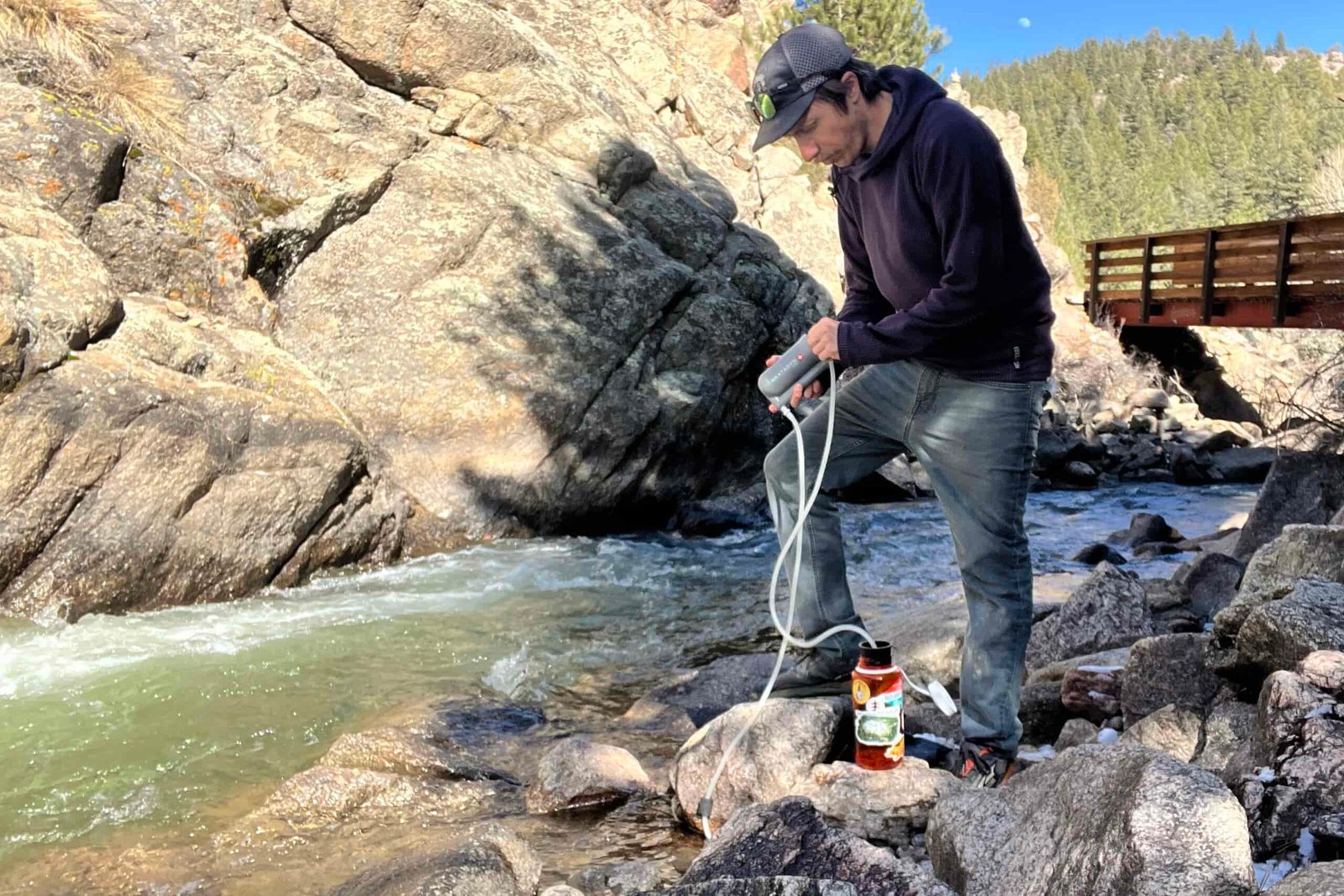 A hiker stands next to a creek and pumps water into a nalgene with the katadyn hiker filter.