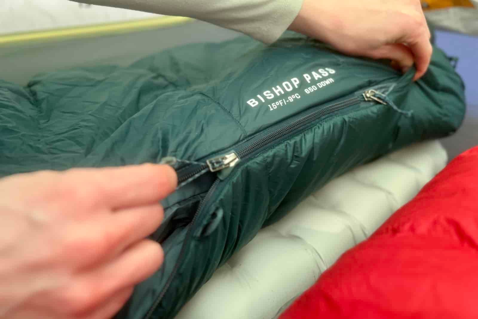 A closeup of a hiker zipping up a sleeping bag