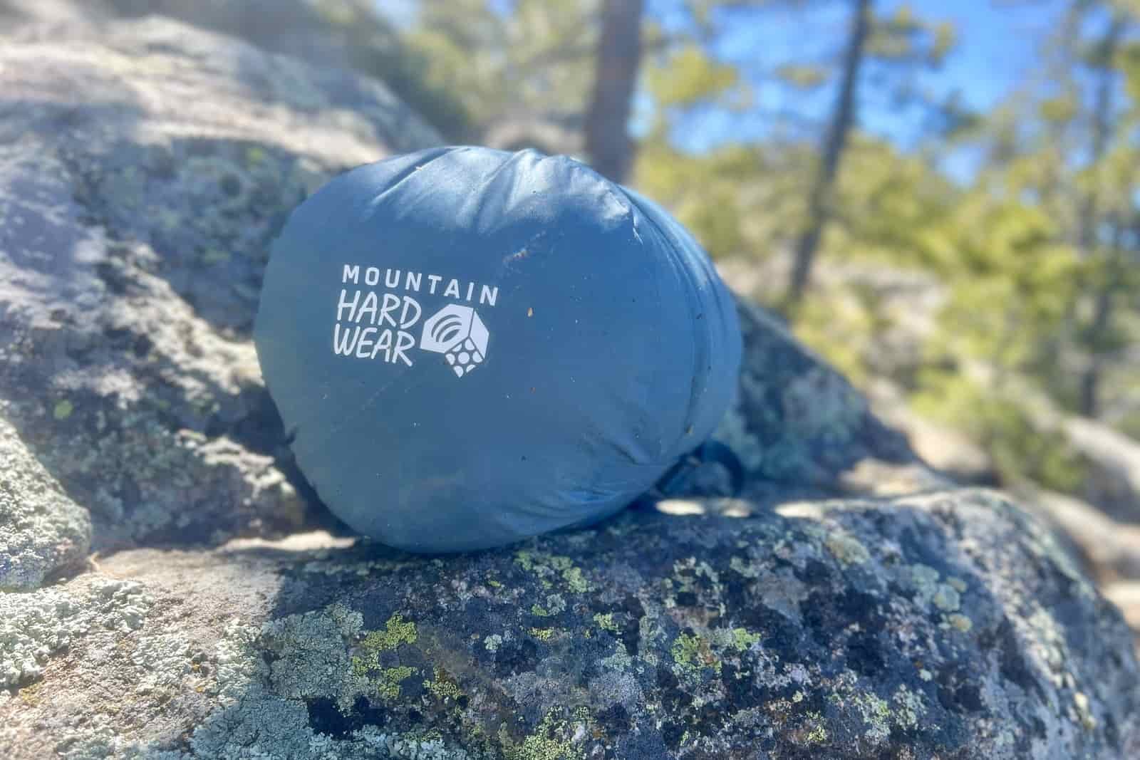 A sleeping bag packed in a compression sack sits on a rock