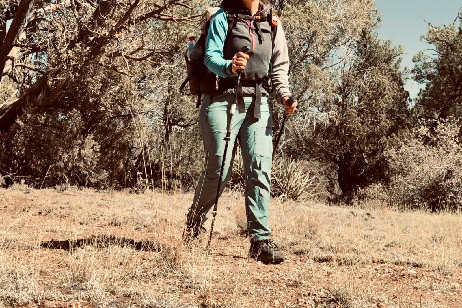A hiker wearing a backpack and the Baleaf pants walks down a trail in the woods.