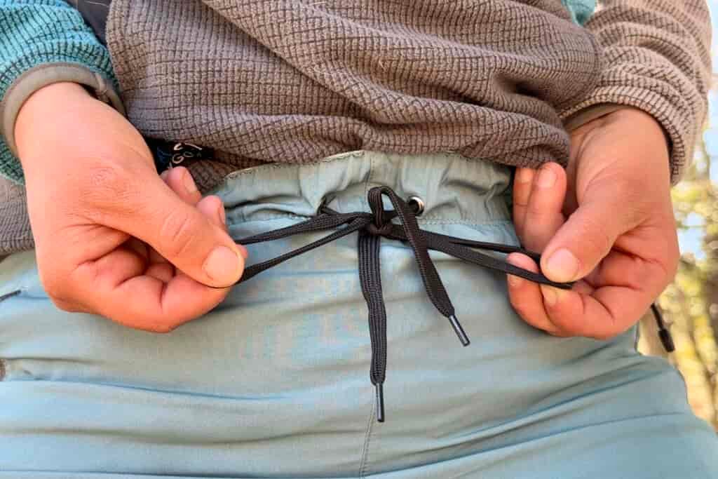 A close up of a person tying the drawstring of the Baleaf pants.