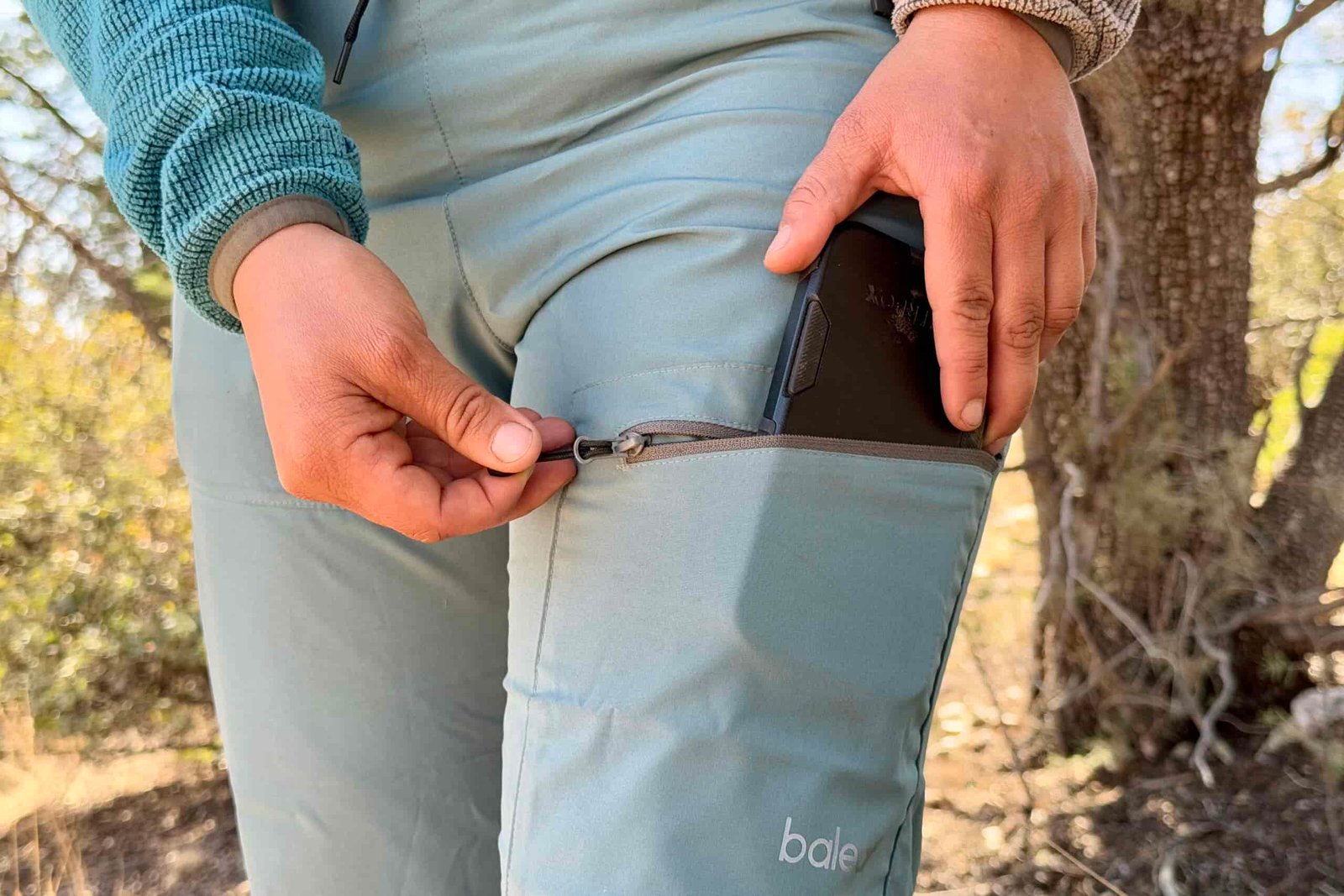 A close up of a person is putting a phone into the leg pocket of the Baleaf pants.