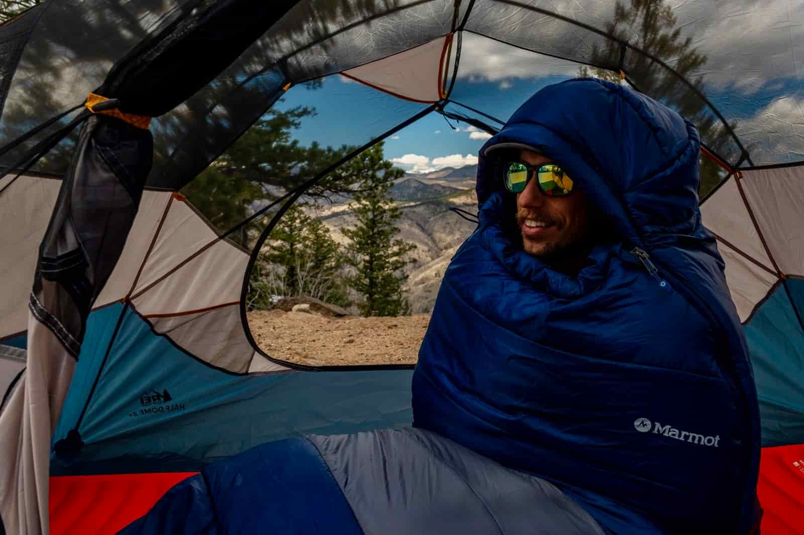 A hiker sits up in a sleeping bag in a tent