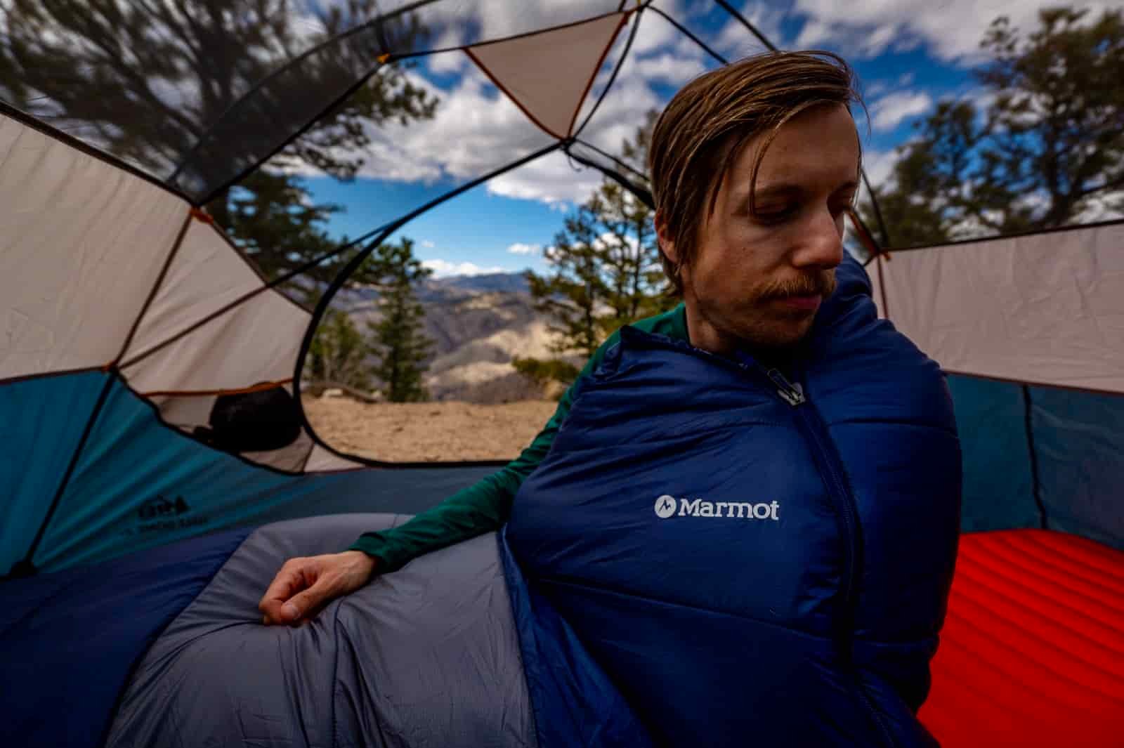 A hiker sits up in a sleeping bag in a tent
