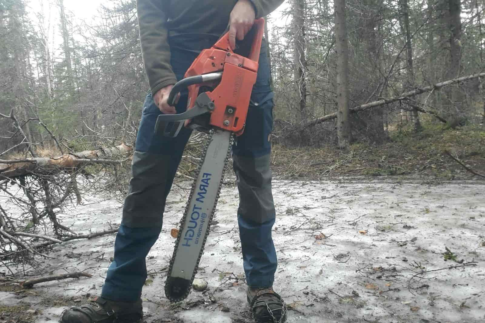A man stand with a chainsaw on an icy trail.