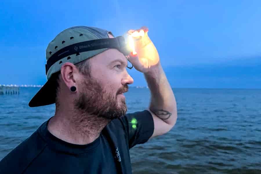 A man adjusting the headlamp on his head with the ocean in the background.
