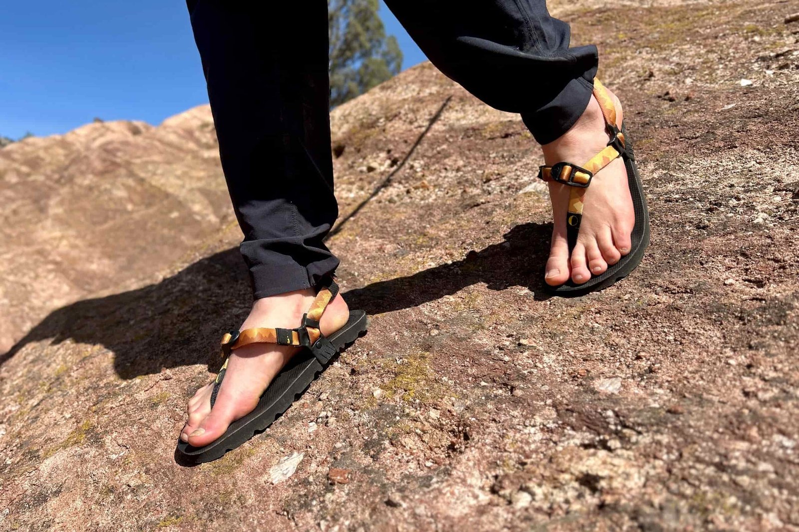 Close up image of a person descending a steep rocky slope in sandals