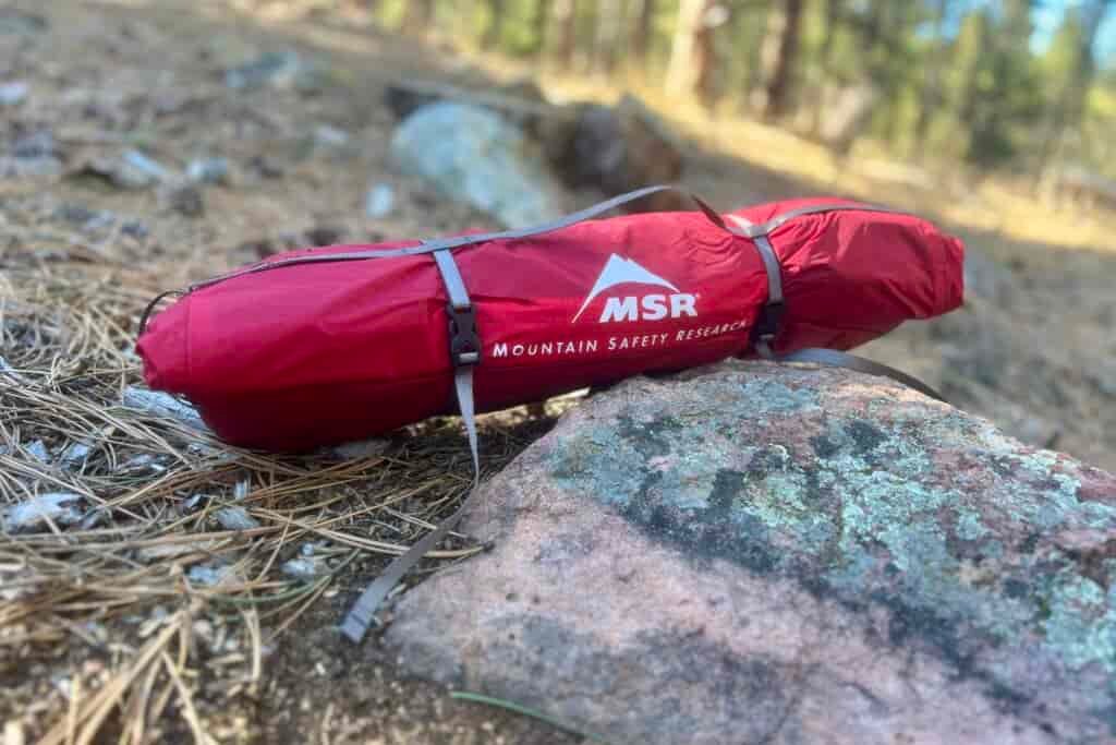 a red msr tent sits packed up on a rock