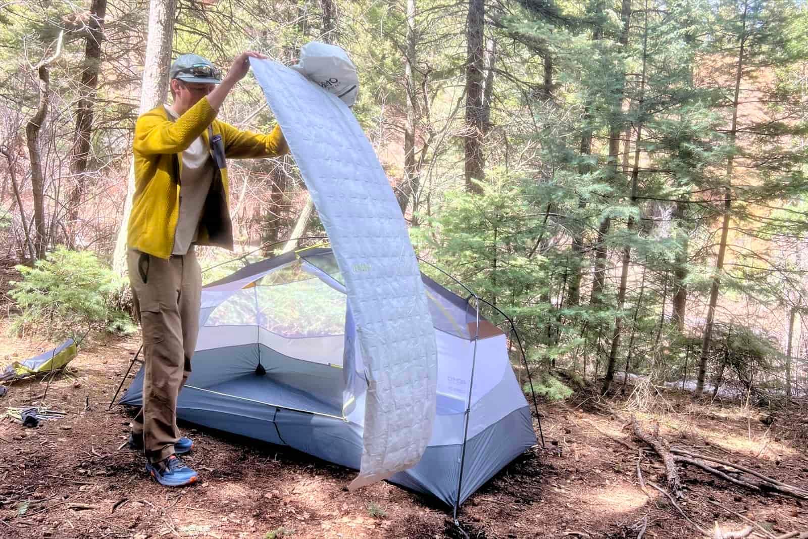 a hiker tosses a deflated gray sleeping pad next to a tent