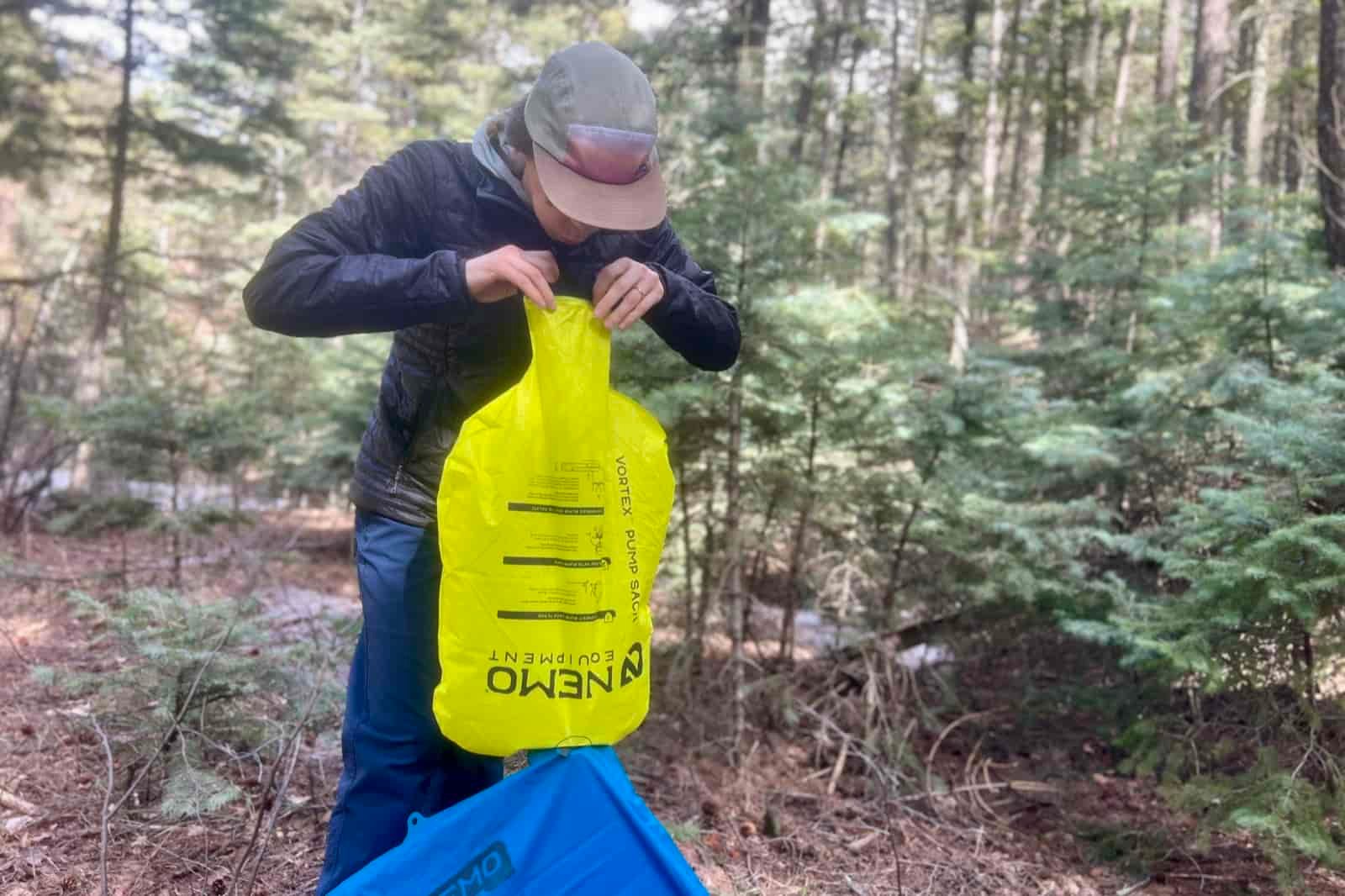 a hiker blows into a pump sack attached to a blue sleeping pad