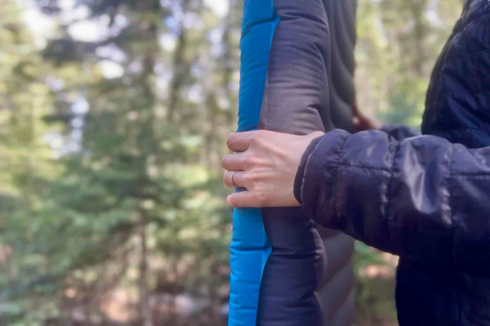 a close up of a hiker grasping the thickness of a blue sleeping pad