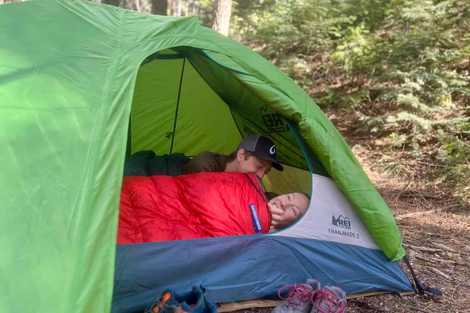two hikers lay down in a green tent