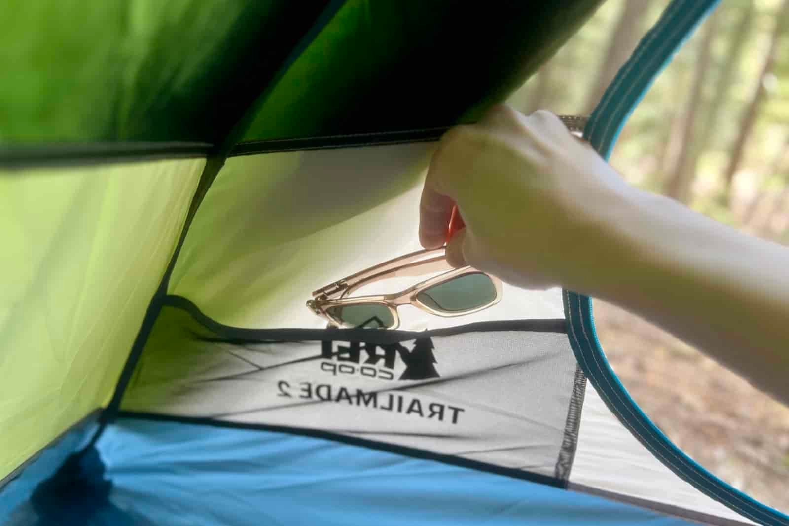 a hand stuffs a pair of sunglasses into a mesh pocket in a tent