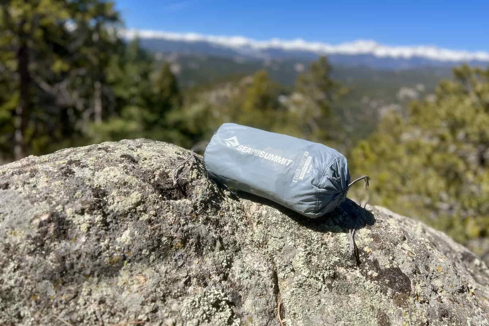 a grey stuff sack containing a sleeping pad sits on a rock