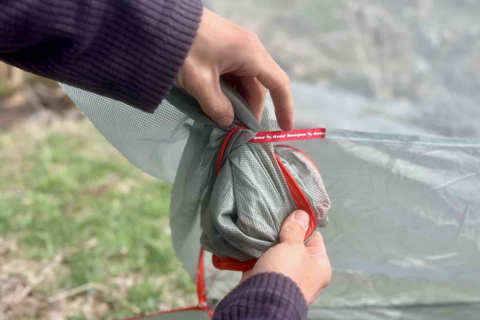 a close up of a hiker stuffing the door of a tent into its door keeper
