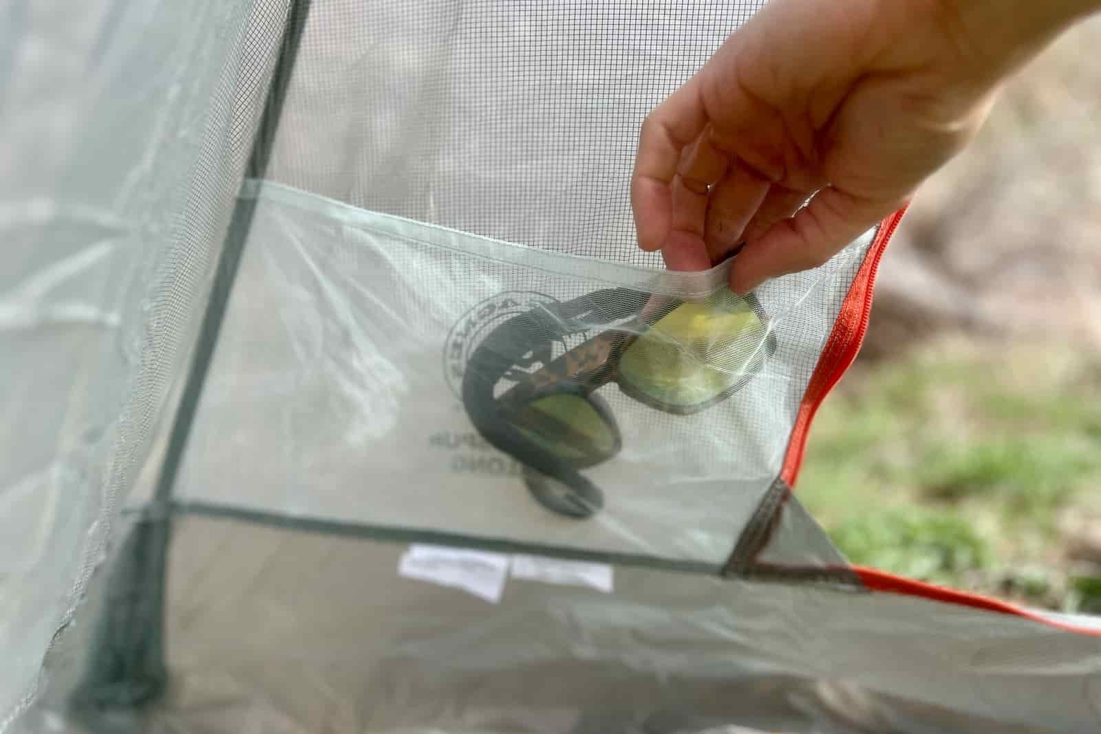 aa close up of a hiker stuffing a pair of sunglasses into the mesh pocket of a tent