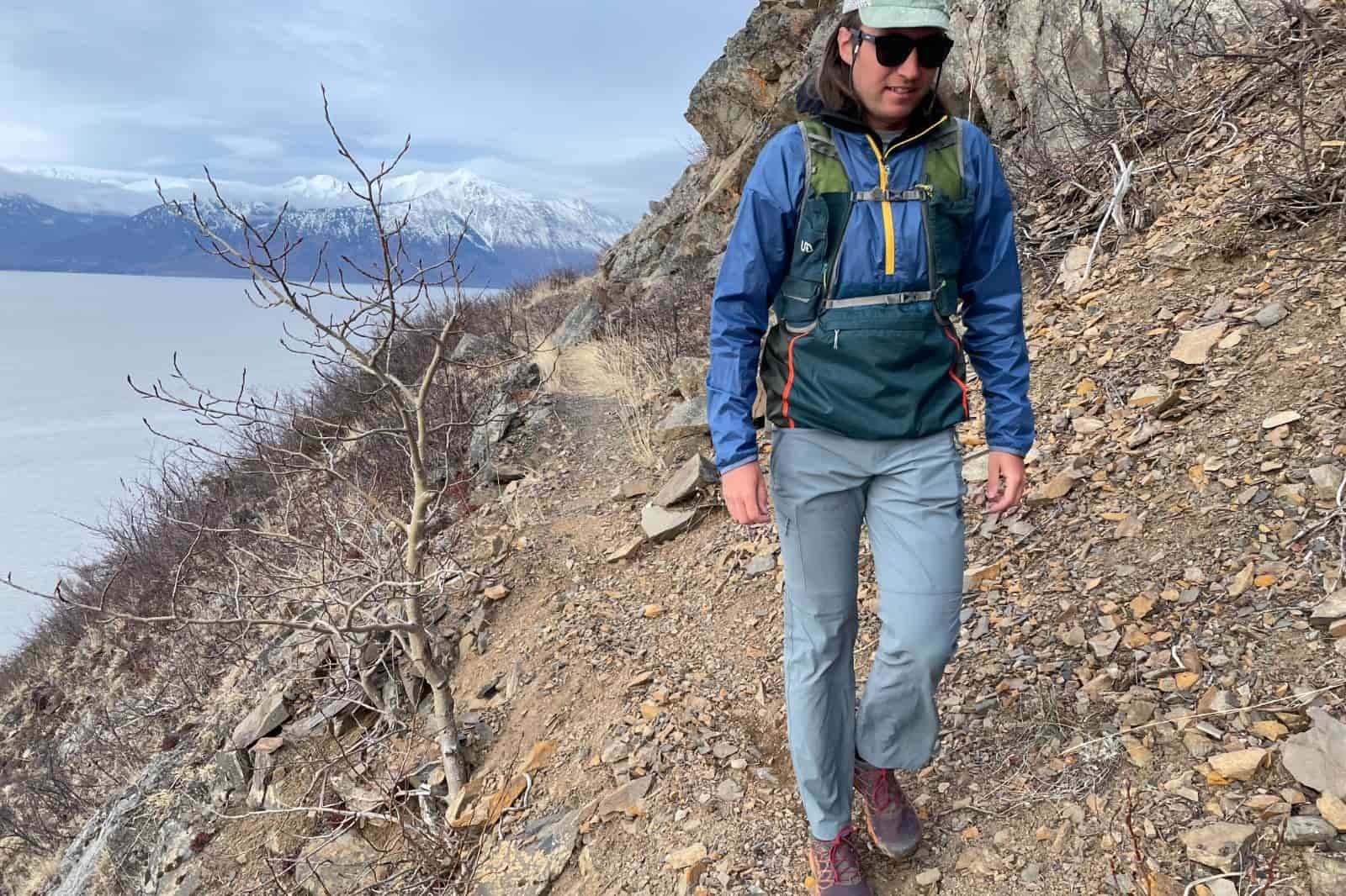 A man walks along a narrow trail above the ocean.