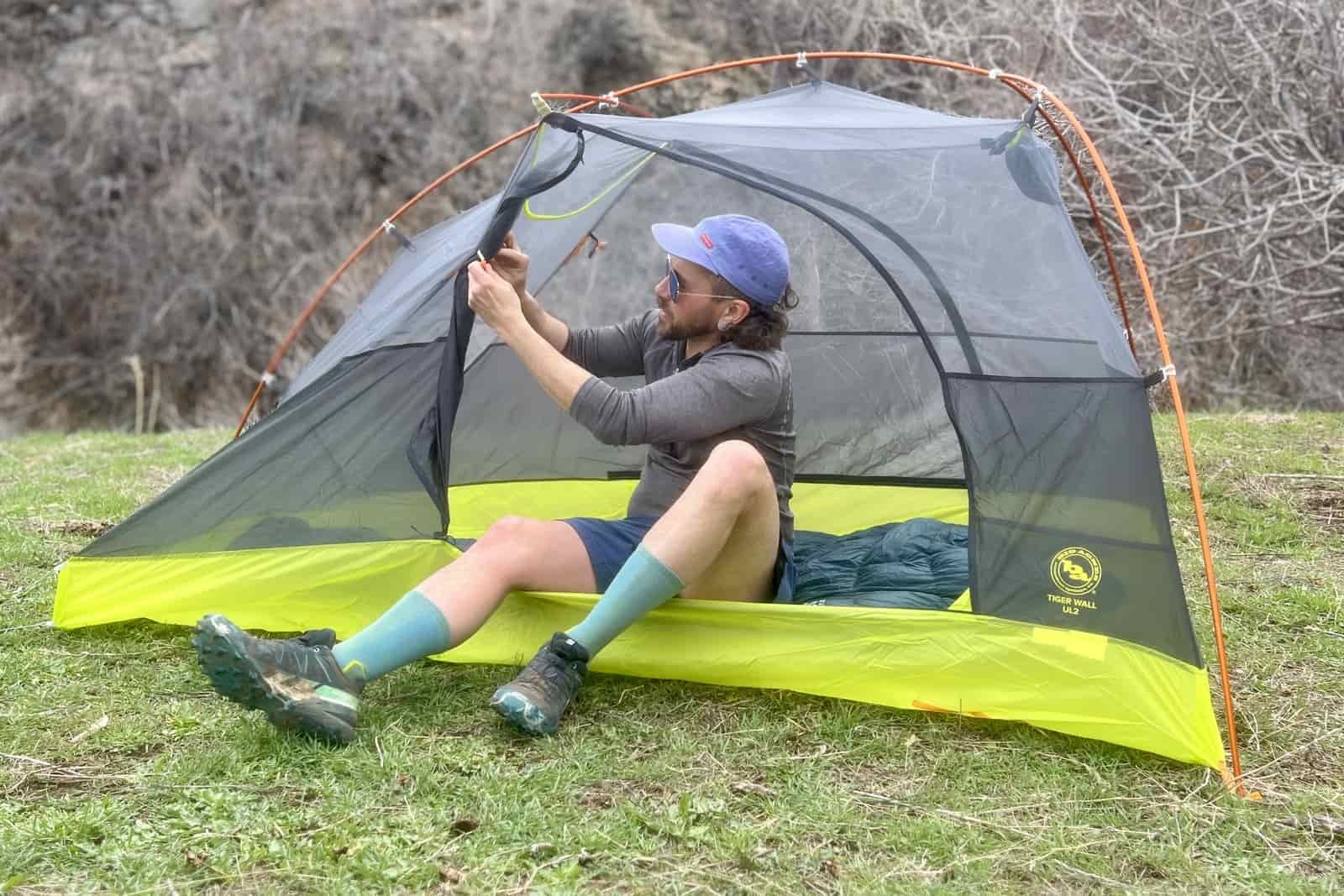 a hiker sits in a tent and ties back the door
