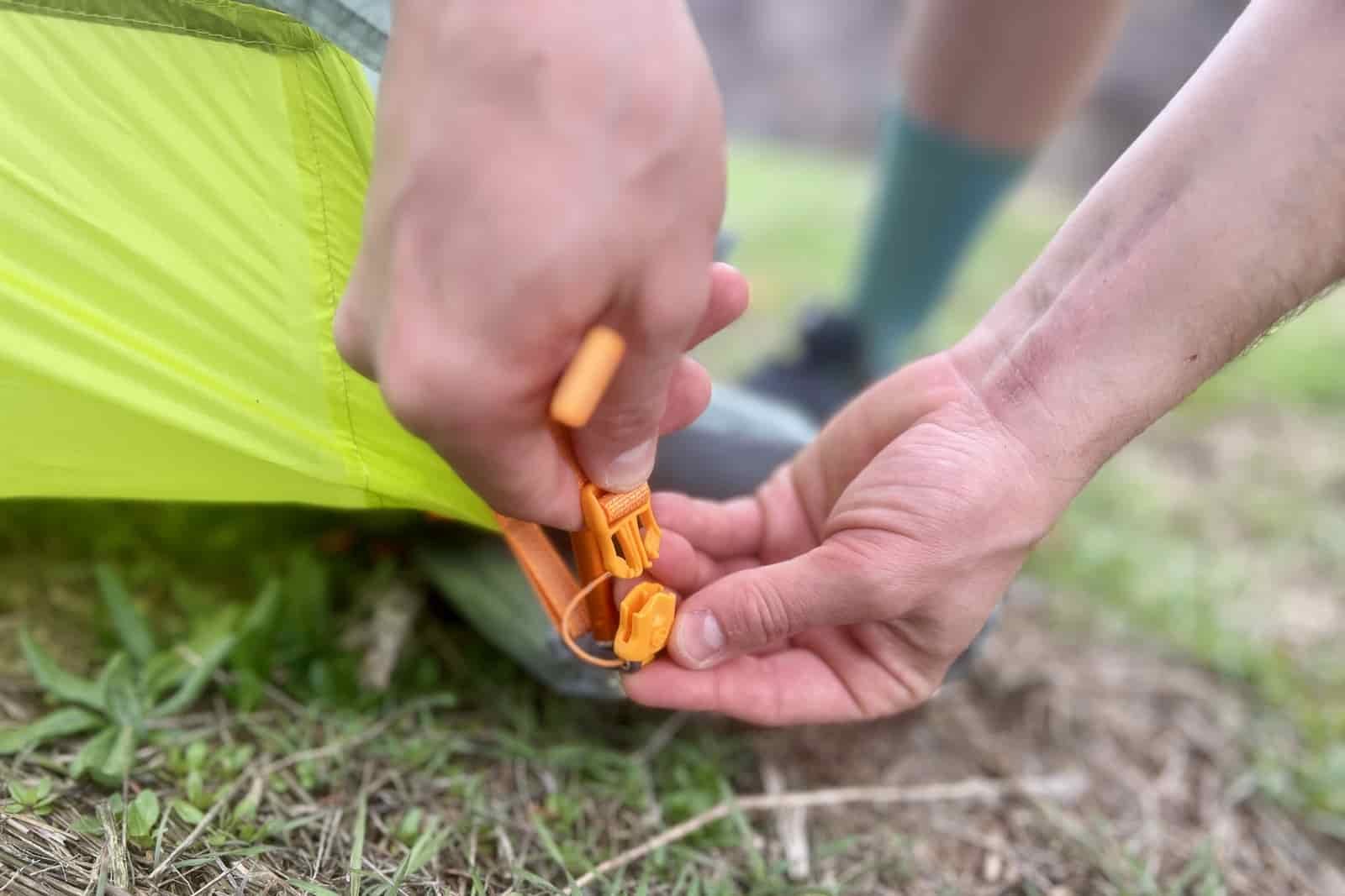 a close up of hands attaching a tent rainfly to a tent