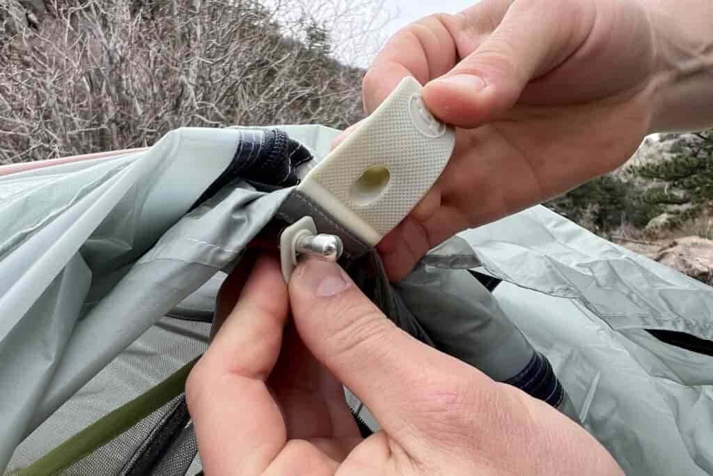 a close up of hands showing the rainfly connecton point on a tent