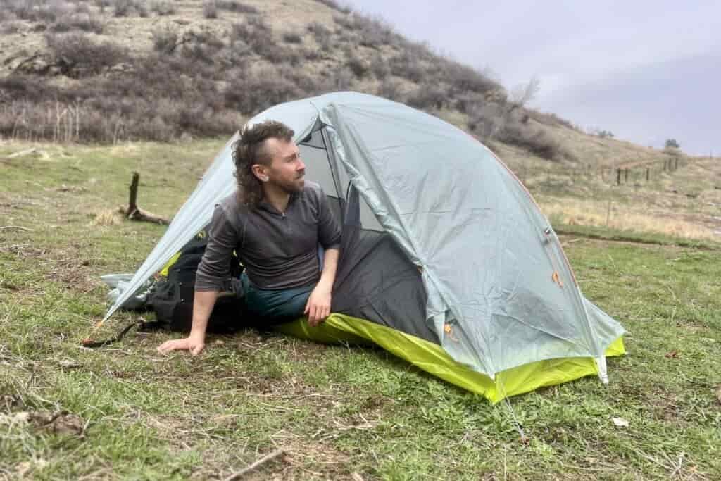 a hiker leans out of a light grey tent