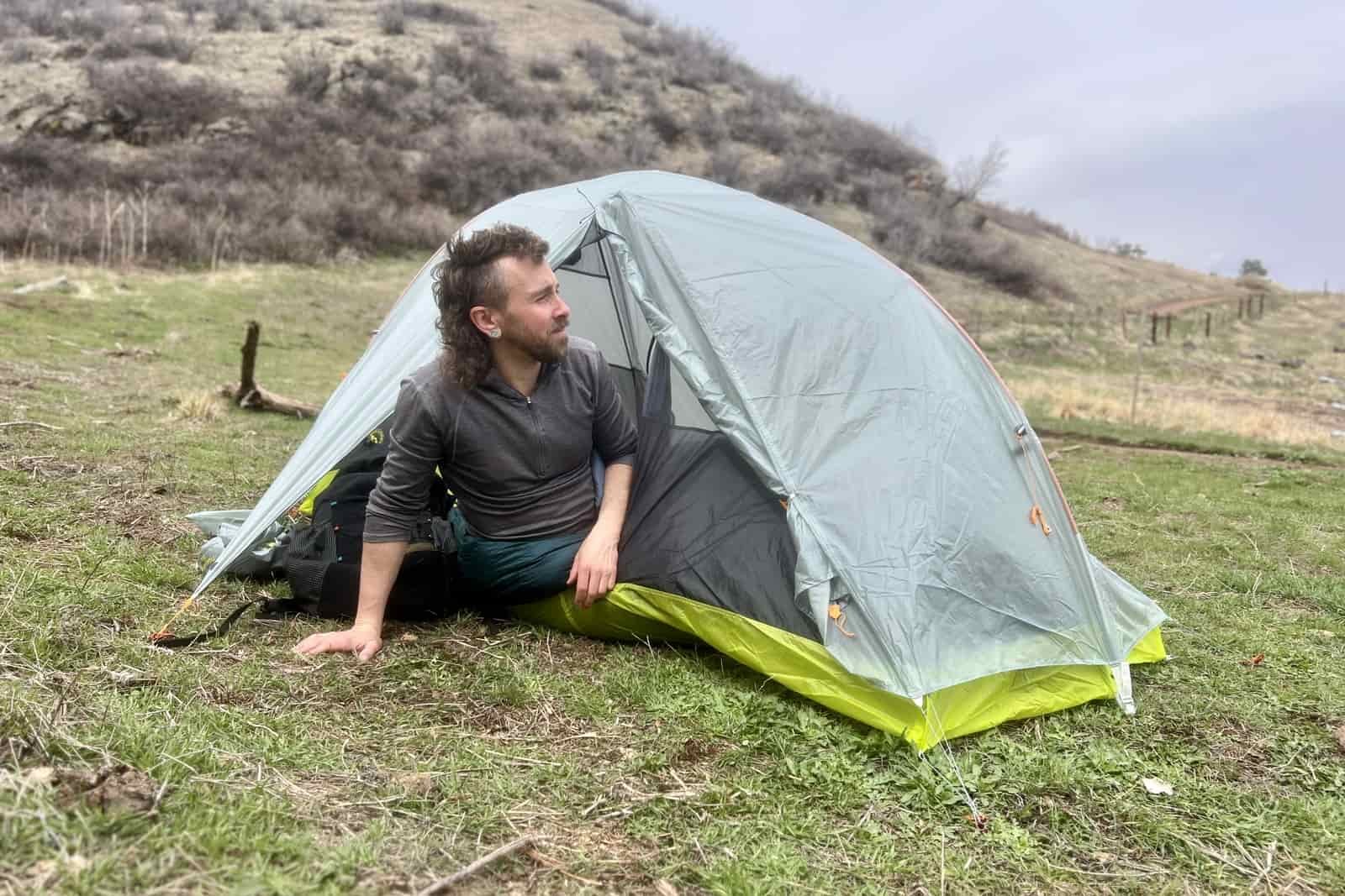 a hiker leans out of a light grey tent