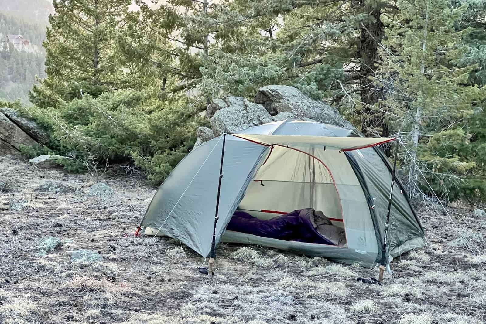 a tent is pitched in the forest with the awning deployed and the door open