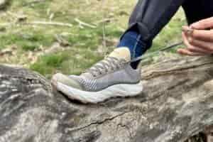 Close up image of a person tying the shoelaces on a pair of trail runners while sitting on a log.