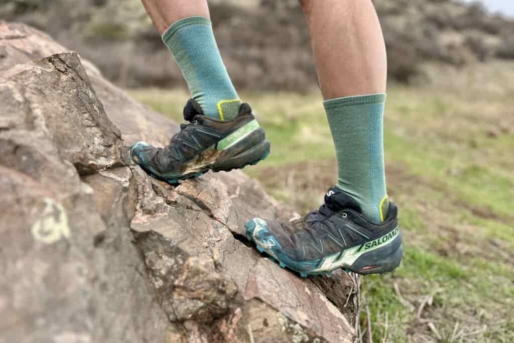 Close up from the knees down of a man climbing up a steep rock.