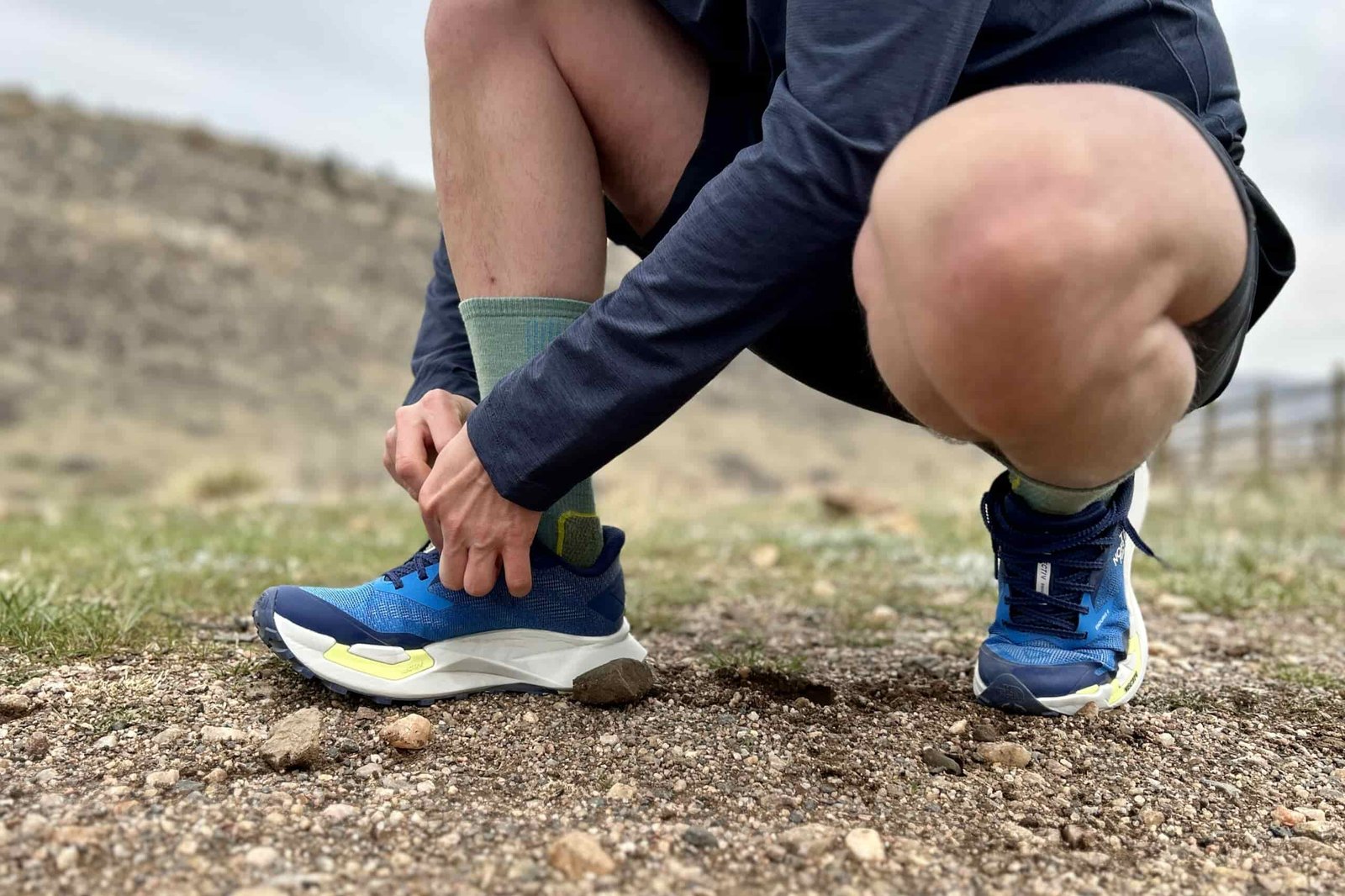 Close up image of a man from the waist down adjusting a pair of trail runners.