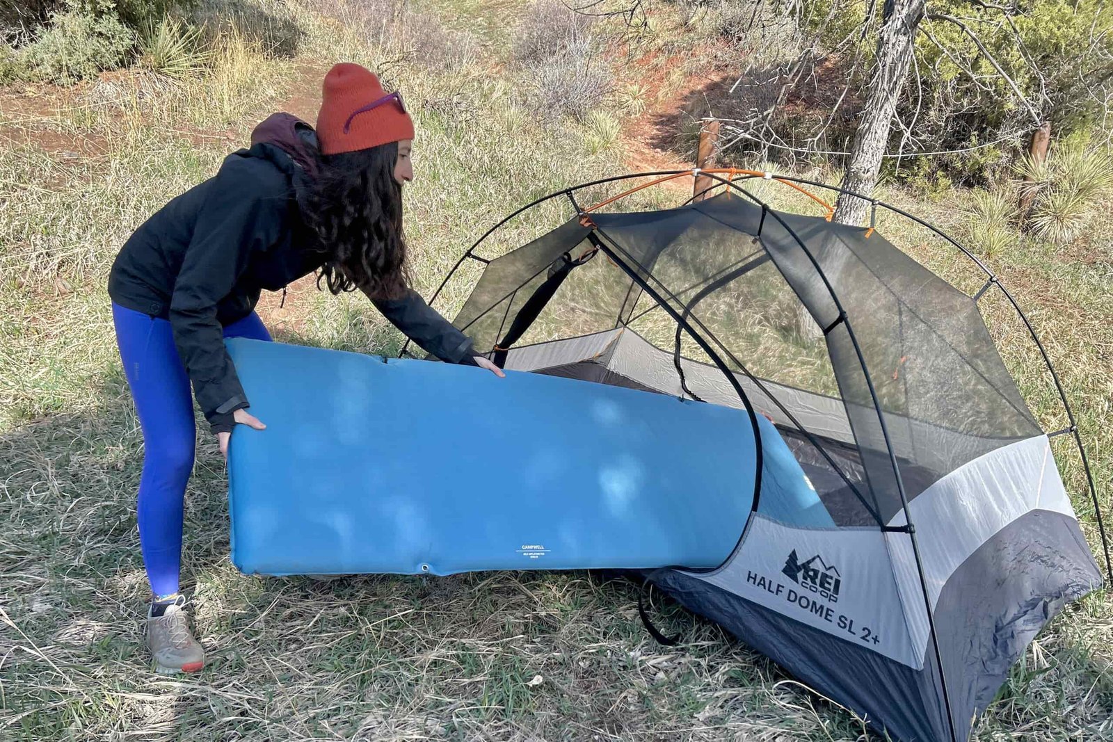A woman puts a sleeping pad inside a tent in a wilderness setting.