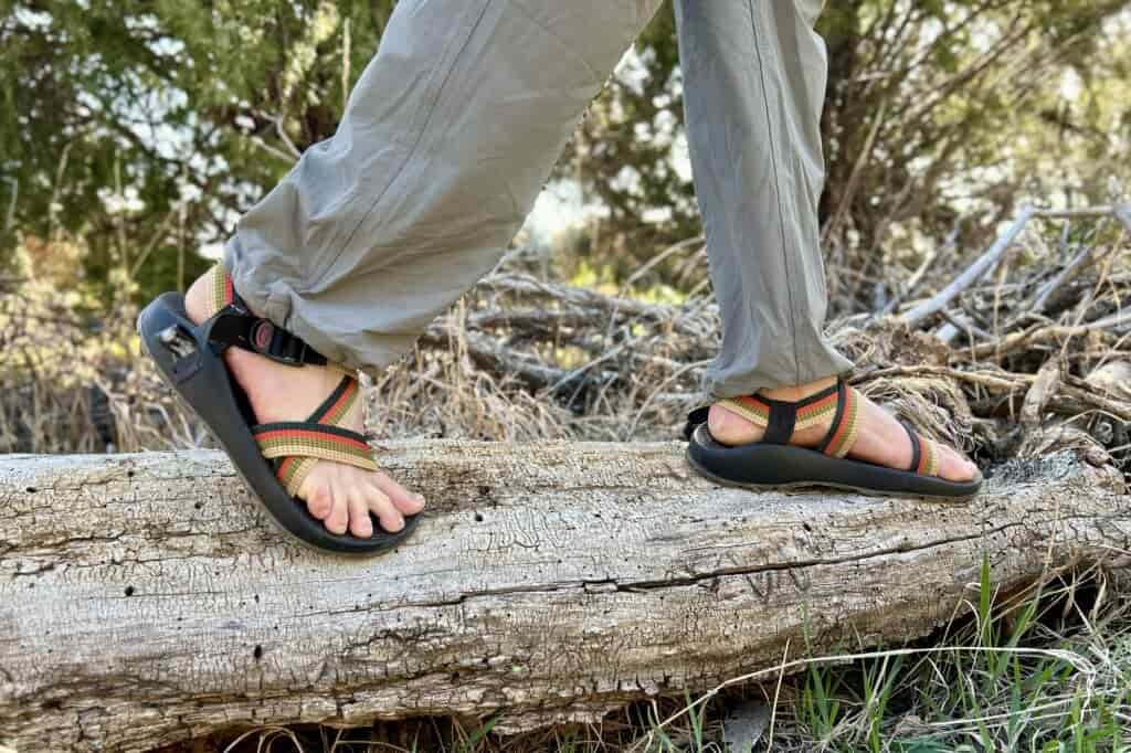 Close up image from knees down of a person walking across a log in sandals