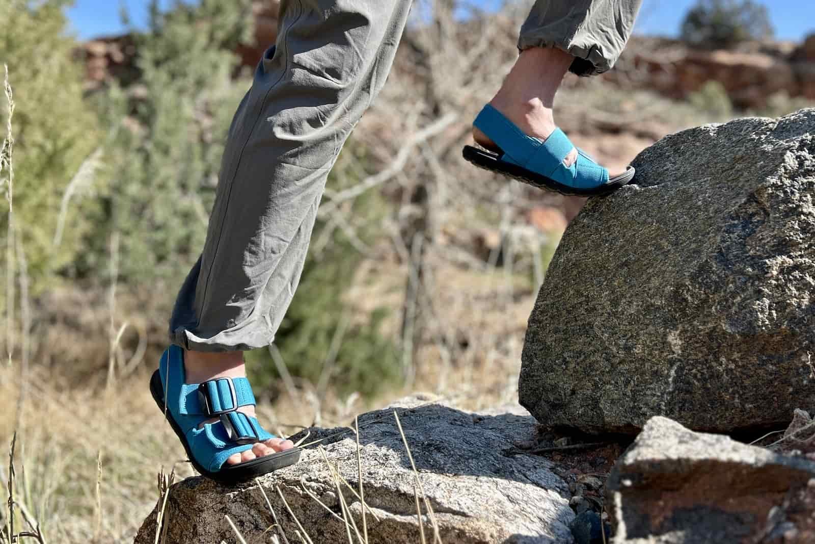 Close up image from the knees down of a person climbing up steep rocks in a forested setting.