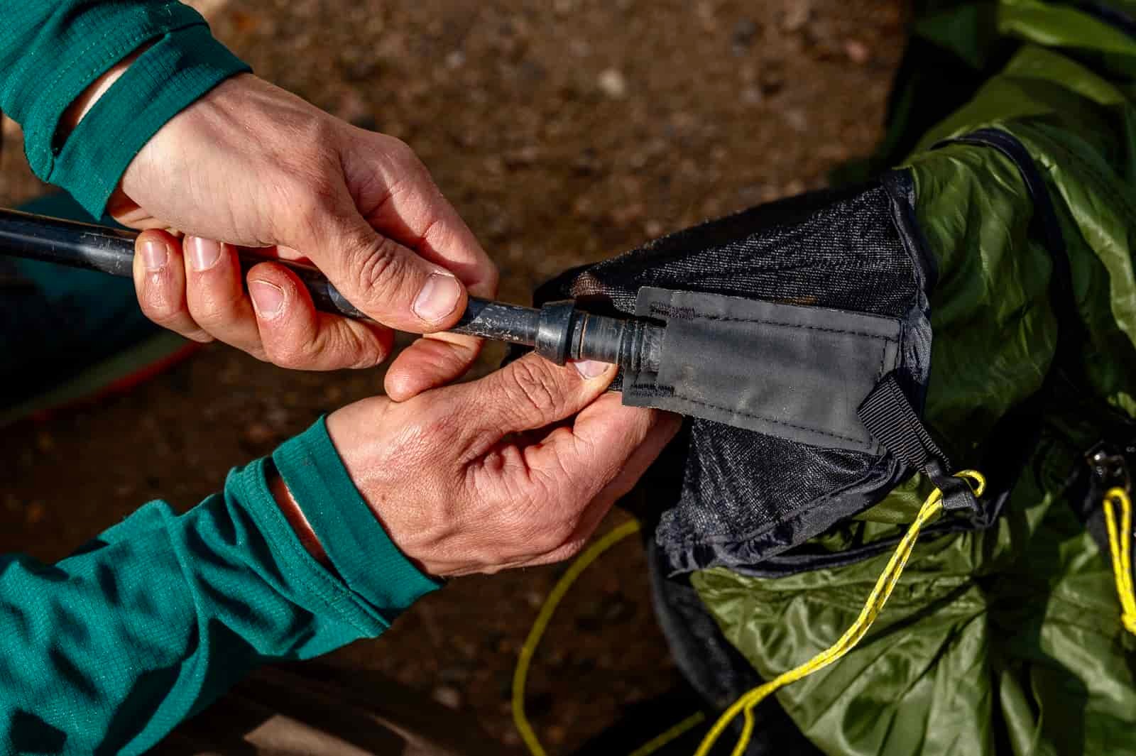 A close up of a hiker inserting a trekking pole into the trekking pole inserts of a trekking pole tent.